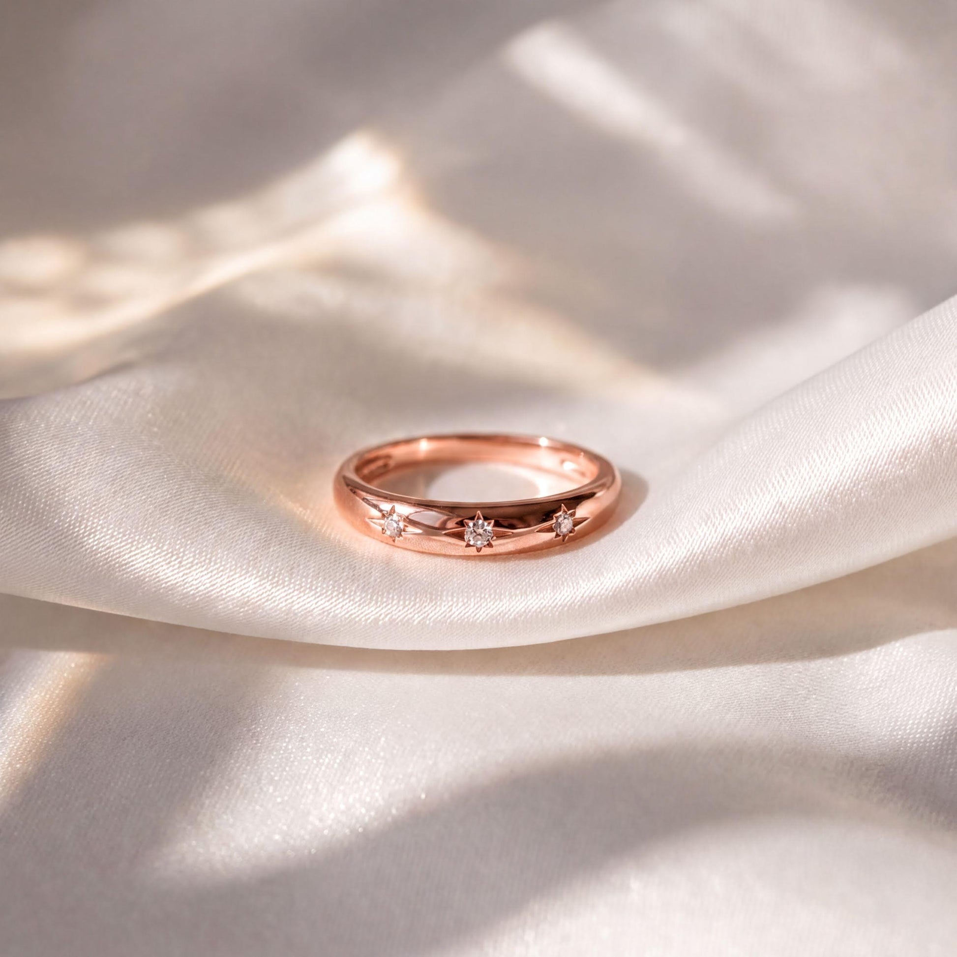 A gold ring with three small diamonds is resting on a white fabric surface.
