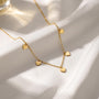 A delicate gold necklace with small heart-shaped charms dangles from a white fabric surface, creating a romantic and elegant appearance.