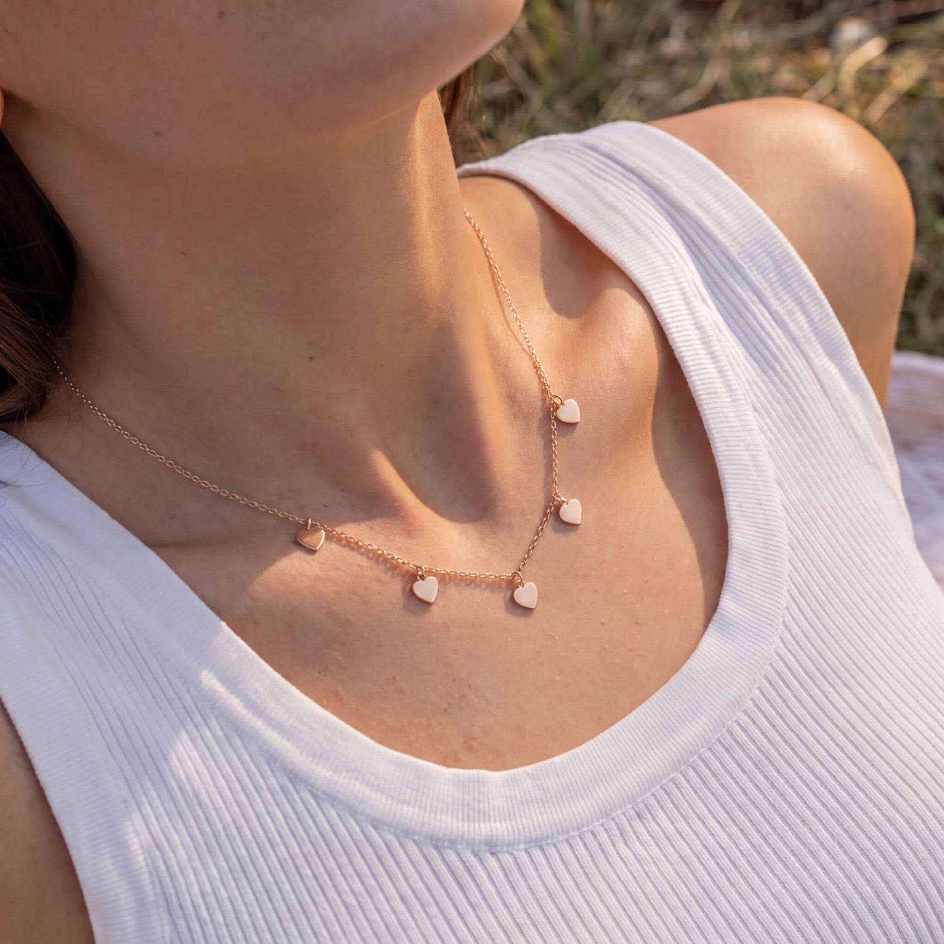 A close-up view of a woman wearing a necklace with small heart-shaped charms.