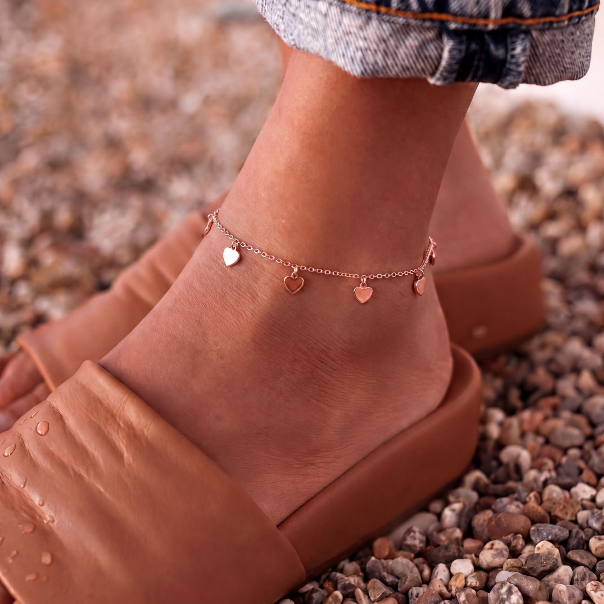 A close-up of a person's ankle wearing a charm bracelet with heart-shaped charms.