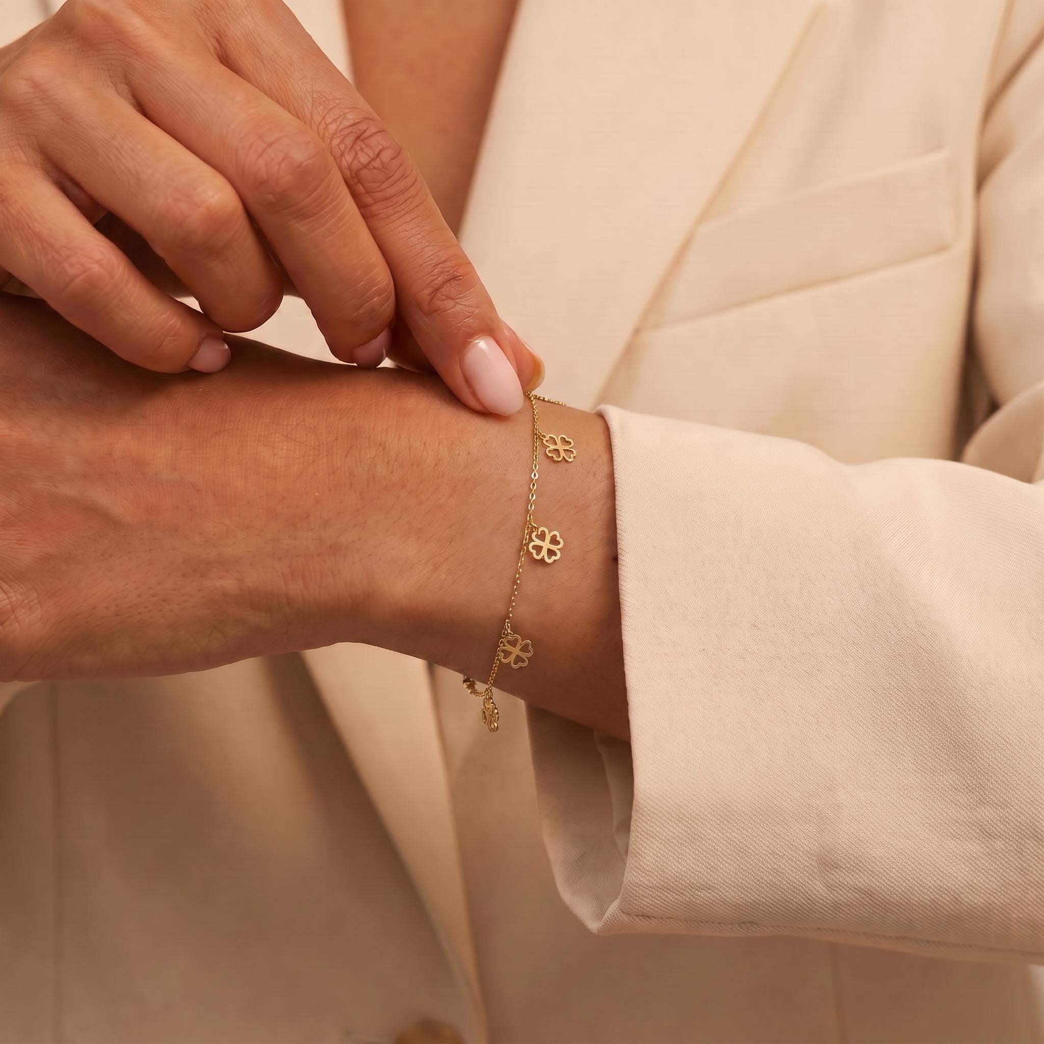 A close-up image of a person's hand wearing a gold bracelet with small flower charms.