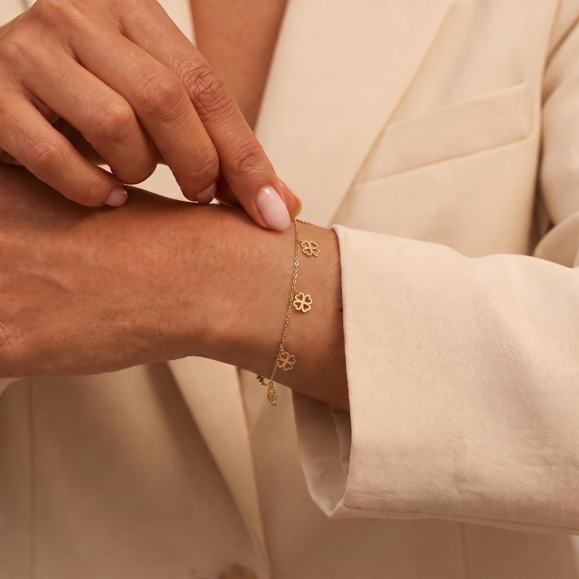 A close-up image of a person's hand wearing a gold bracelet with small flower charms.