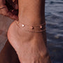 A close-up view of a person's ankle wearing a delicate gold-colored ankle bracelet with small heart-shaped charms.