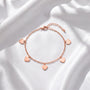 A delicate gold-colored bracelet with small heart-shaped charms attached to it, resting on a white fabric background.