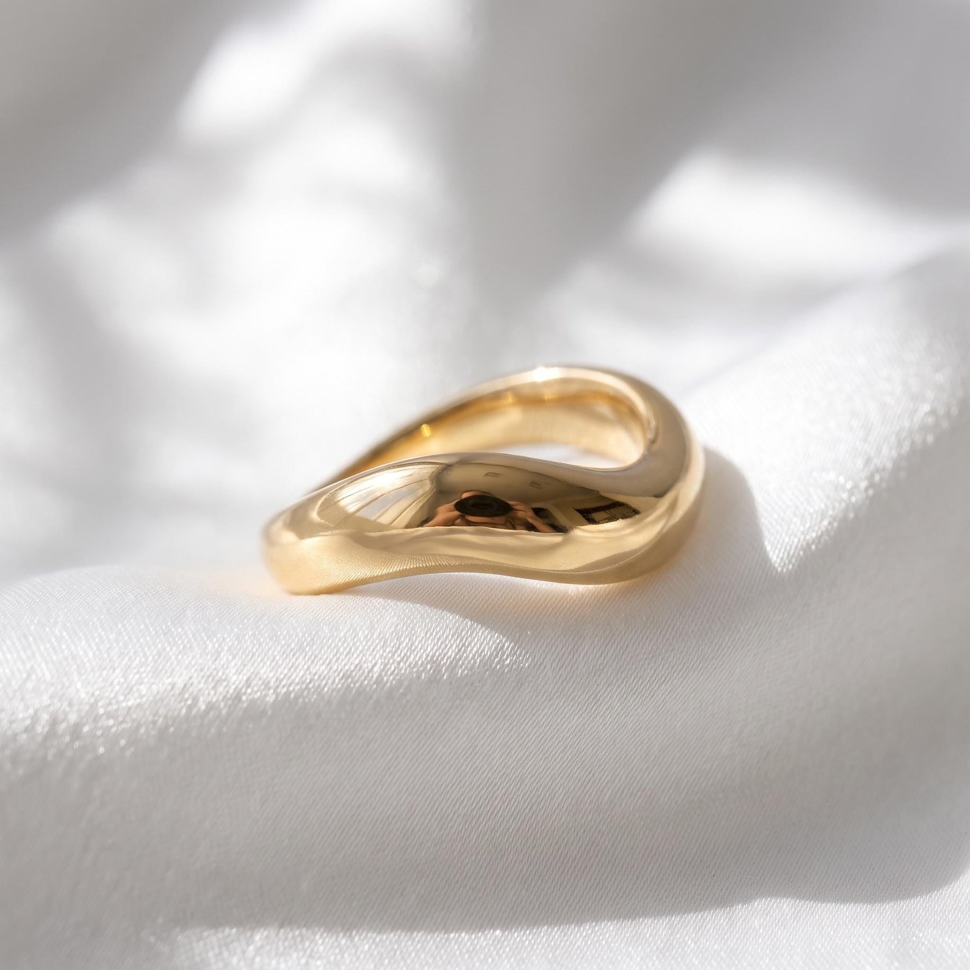 A gold ring with a curved design rests on a white fabric surface.