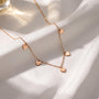 A delicate gold necklace with small heart-shaped charms dangles from a white fabric surface, creating a romantic and elegant display.