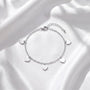 A silver bracelet with heart-shaped charms is displayed on a white fabric background.