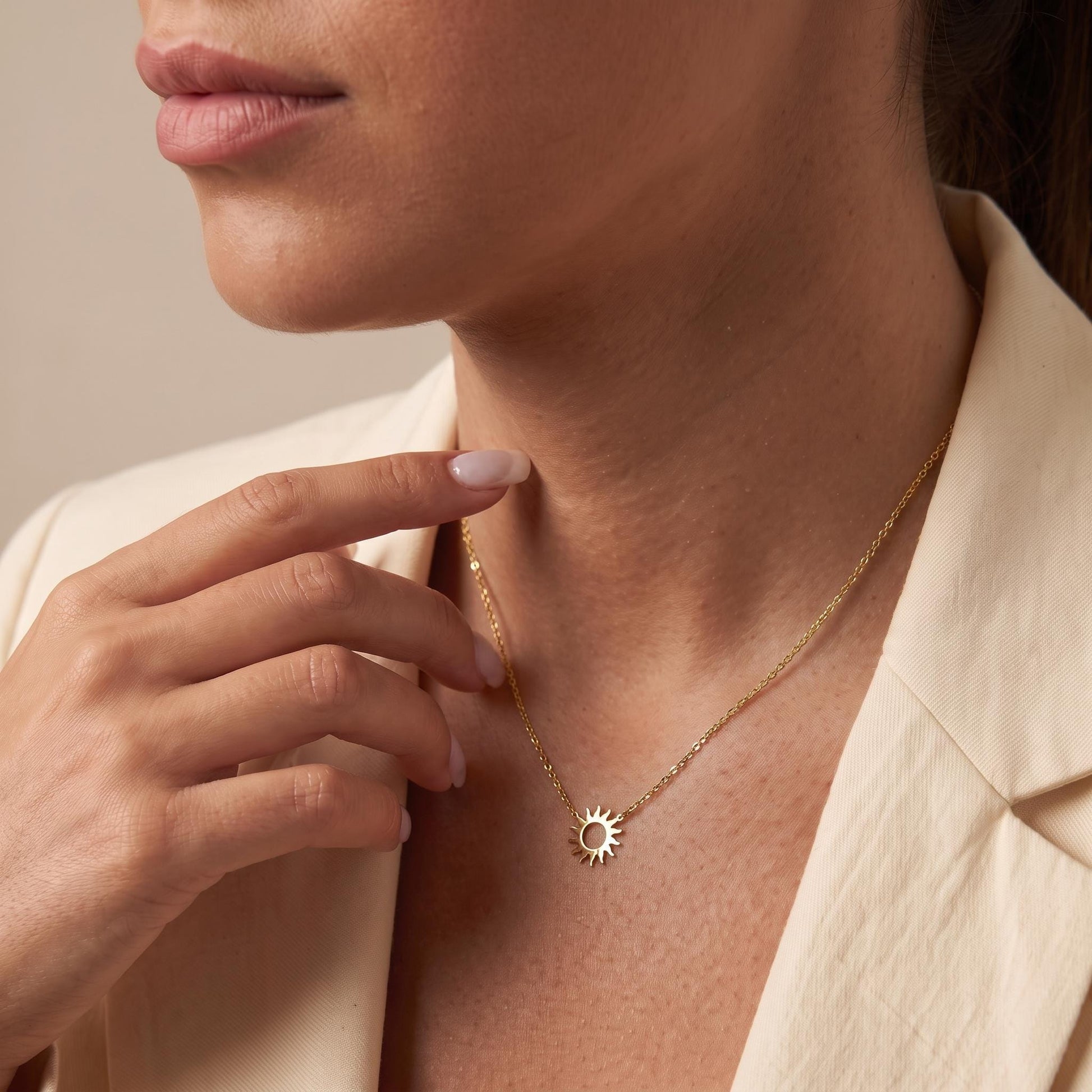 A close-up of a woman's face wearing a gold necklace with a sun pendant.