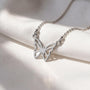 A silver necklace with a butterfly pendant is displayed on a white fabric surface.