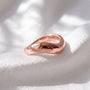 A shiny, copper-colored ring rests on a white fabric surface, its curved shape catching the light.