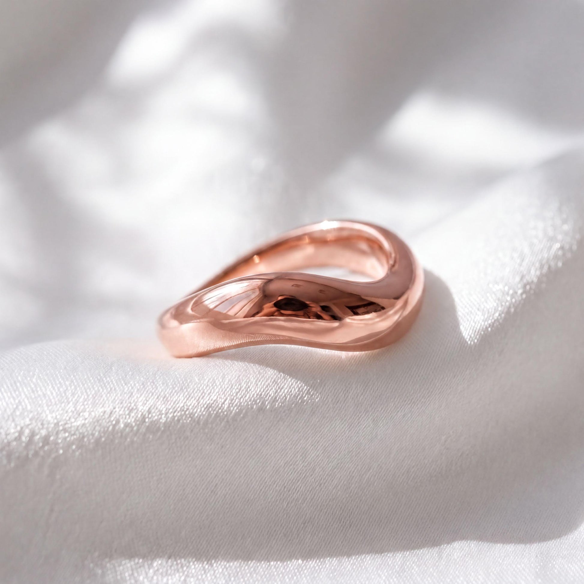 A shiny, copper-colored ring rests on a white fabric surface, its curved shape catching the light.