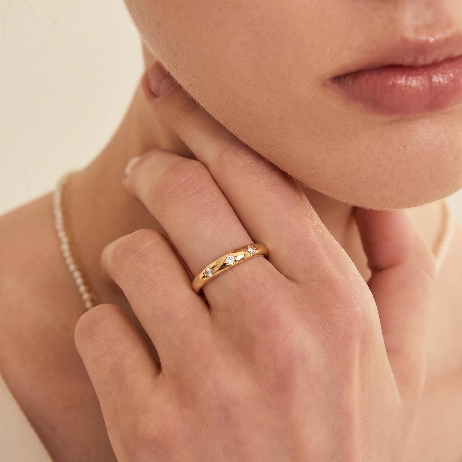 A close-up of a person's hand wearing a gold ring with small diamonds.