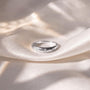 A silver ring with three small diamonds is resting on a white fabric surface.