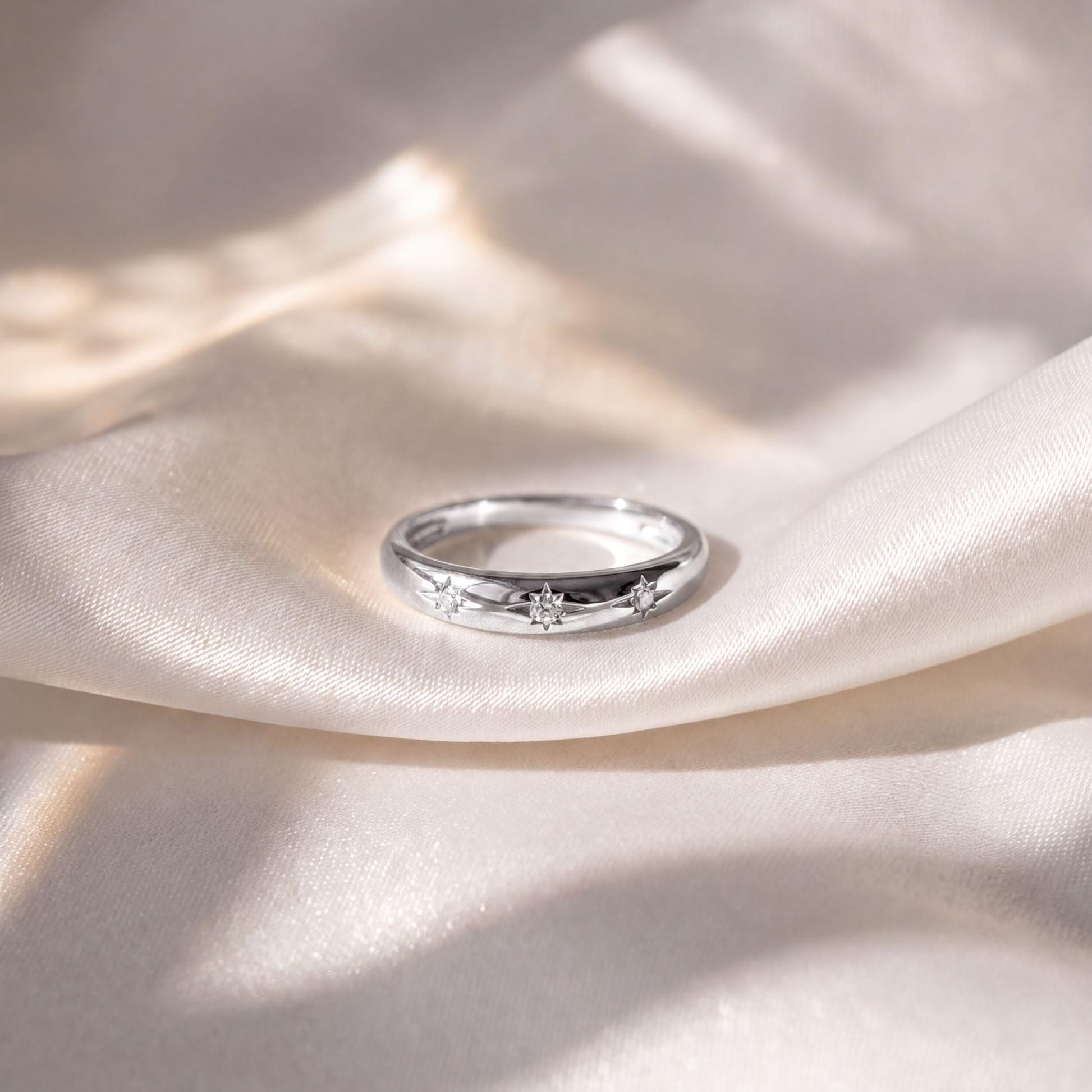 A silver ring with three small diamonds is resting on a white fabric surface.