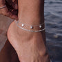 A close-up view of a person's ankle wearing a silver ankle bracelet with heart-shaped charms.