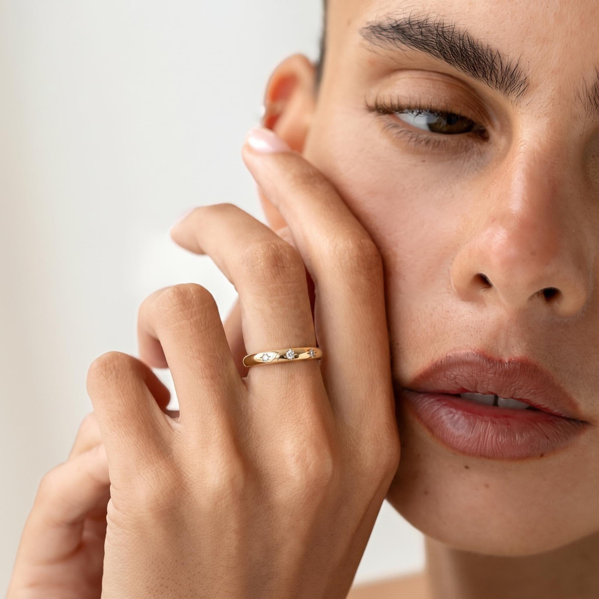 A close-up of a person's face, focusing on their hand and fingers, with a gold ring visible.
