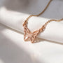 A delicate gold-colored necklace with a butterfly pendant is displayed on a white fabric surface.