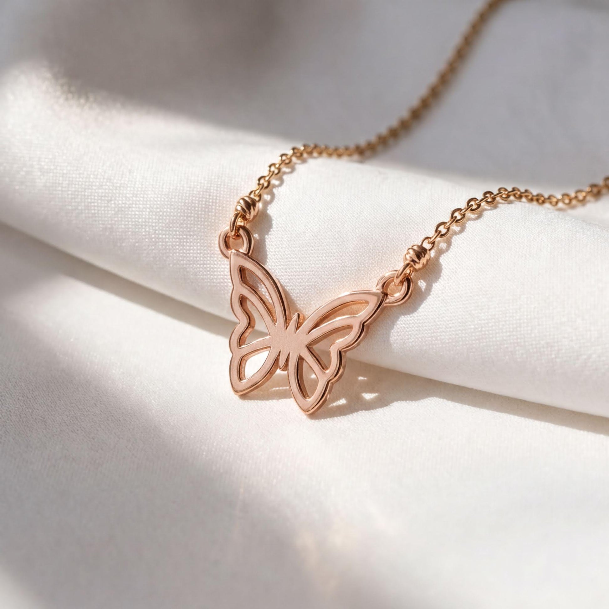 A delicate gold-colored necklace with a butterfly pendant is displayed on a white fabric surface.