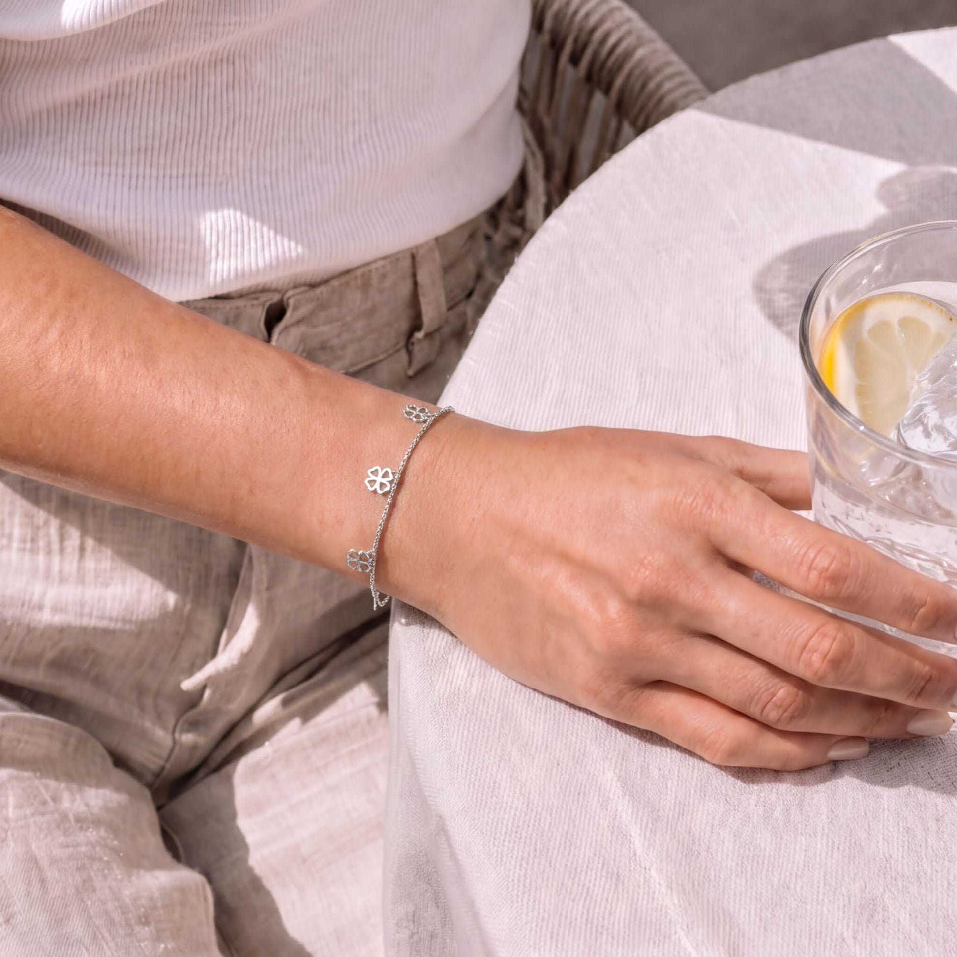 A person's hand wearing a silver bracelet is resting on a table with a glass of water and a lemon slice.