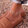 A close-up of a person's ankle wearing a silver ankle bracelet with heart-shaped charms.