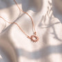 A delicate necklace with a sun-shaped pendant rests on a white fabric surface, casting a shadow on the fabric.