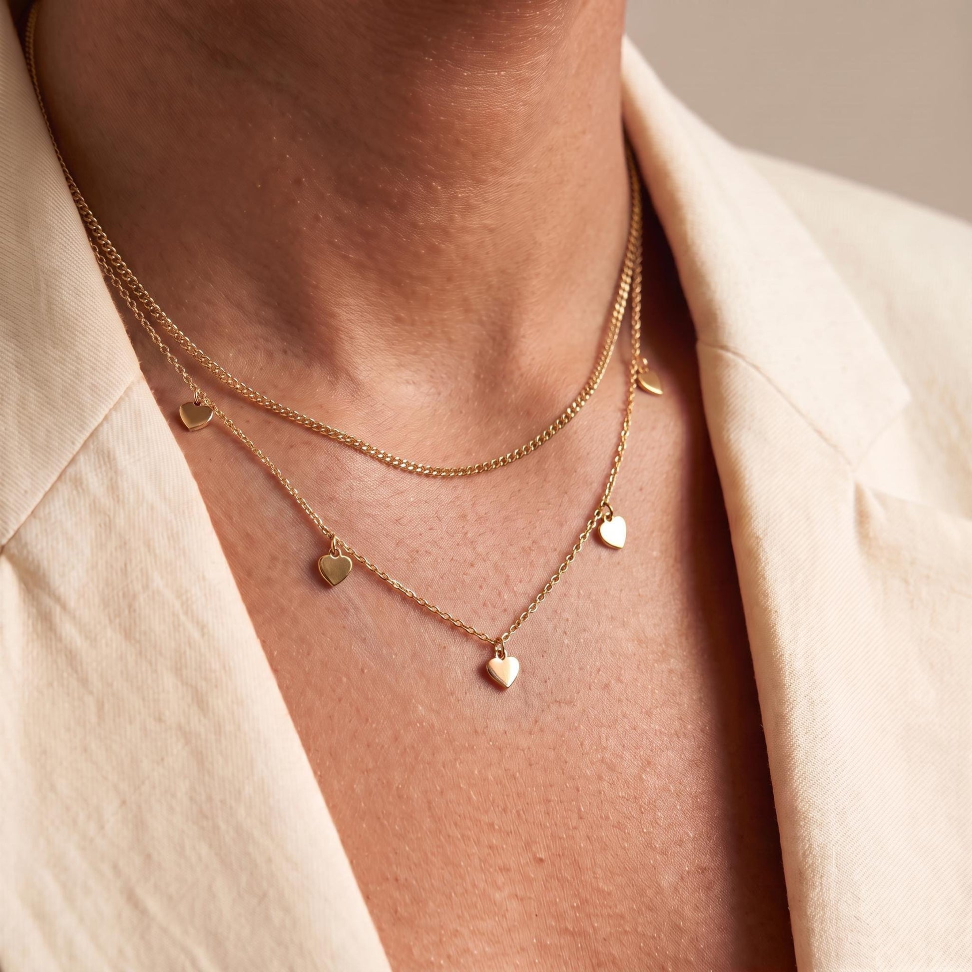 A close-up view of a person's neck and chest area wearing a delicate gold necklace with multiple small heart-shaped charms.