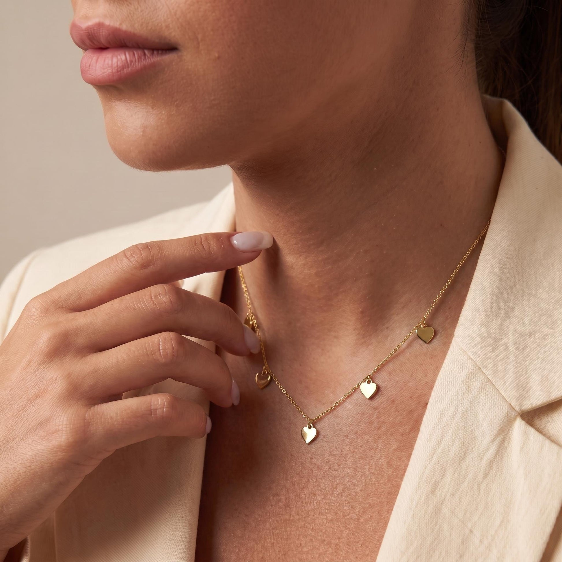 A close-up of a woman's face wearing a gold necklace with small heart-shaped charms.