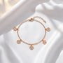 A delicate gold-colored bracelet with four charms, each featuring a four-leaf clover design, is displayed on a white fabric surface.