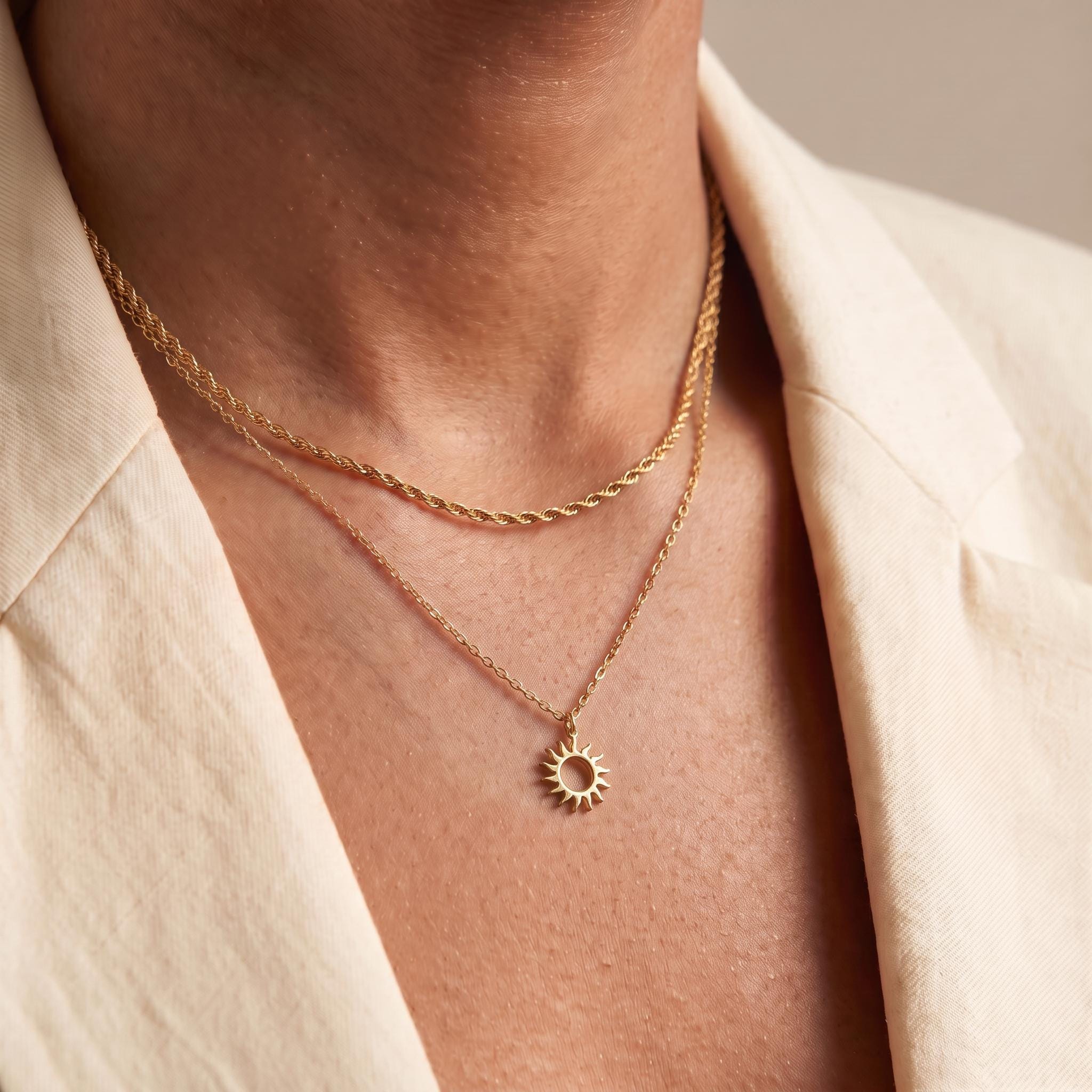 A close-up view of a person's neck and chest area, showing a delicate gold necklace with a pendant featuring a sun design.