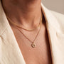 A close-up view of a person's neck and chest area, showing a delicate gold necklace with a pendant featuring a sun design.