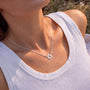 A woman wearing a white tank top and a silver necklace with a sun pendant is shown in the image.