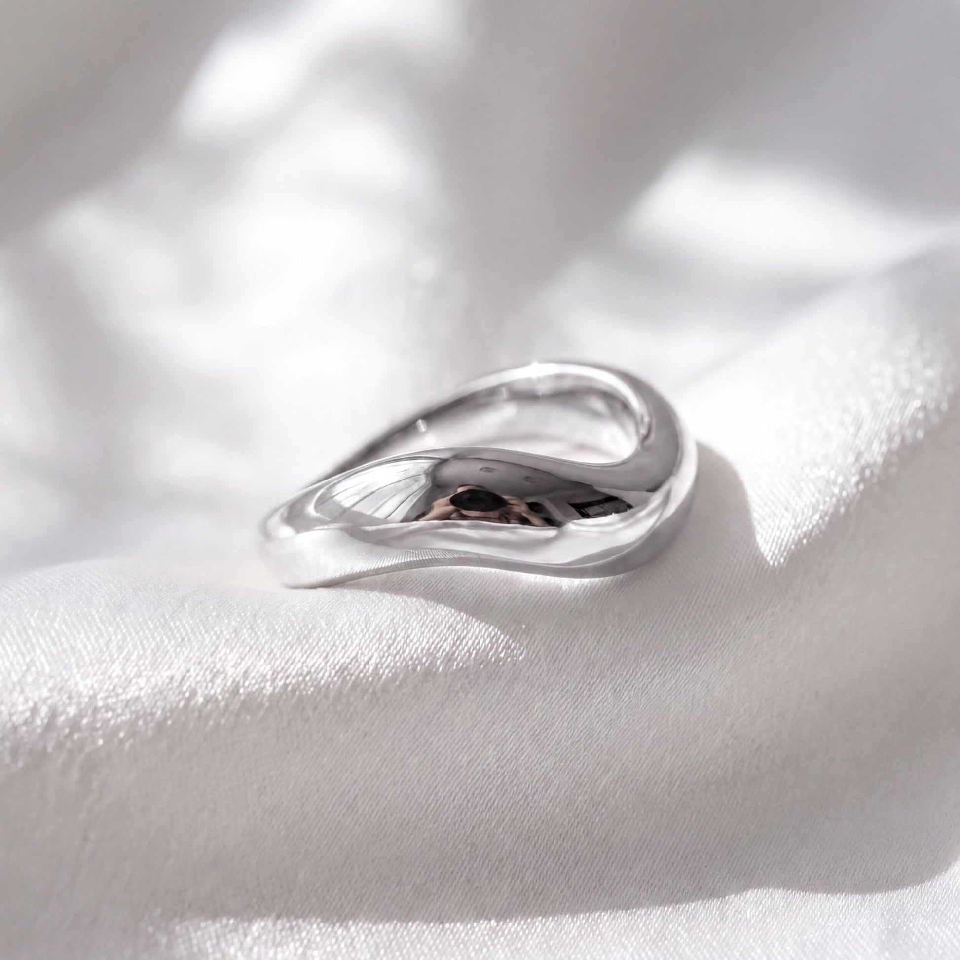 A silver ring with a unique, curved design rests on a white fabric surface.