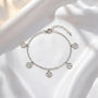 A silver-colored bracelet with four charms hanging from it, placed on a white fabric background.