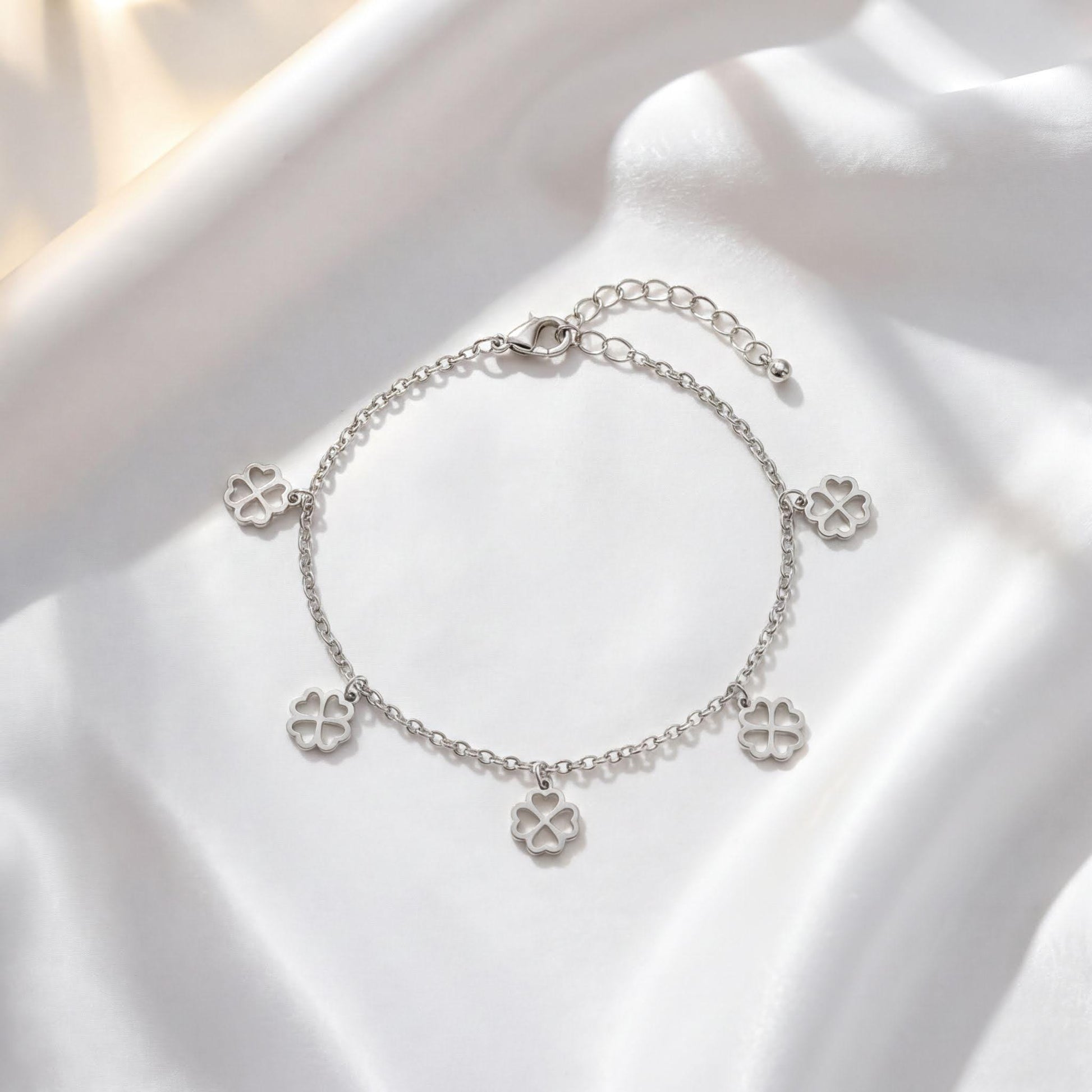 A silver-colored bracelet with four charms hanging from it, placed on a white fabric background.