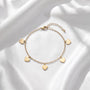 A delicate gold-colored bracelet with small heart-shaped charms attached to it, resting on a white fabric background.