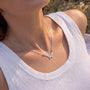 A silver necklace with a butterfly pendant is worn by a person in a white tank top.